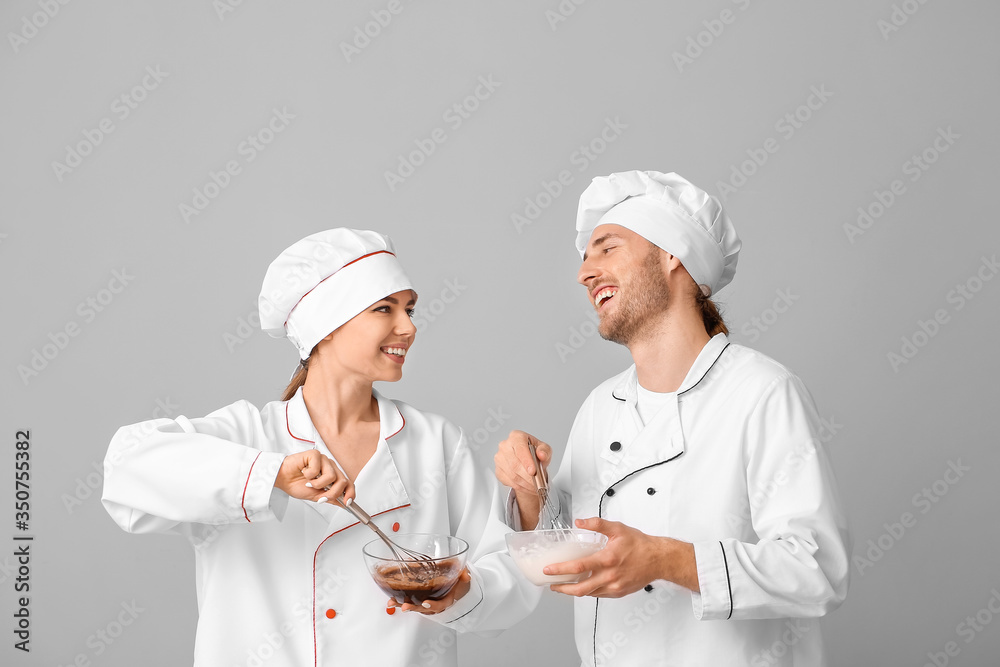 Young confectioners cooking tasty desserts on grey background Young confectioners cooking tasty desserts on grey background