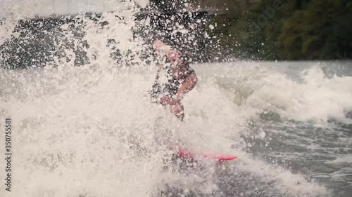 Female wakesurfing spraying water snap on lake slow motion with pink surfboard photo