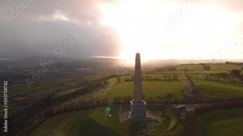 Aerial right to left point of interest drone shot of Knockagh World War Monument during sunset with dark clouds photo