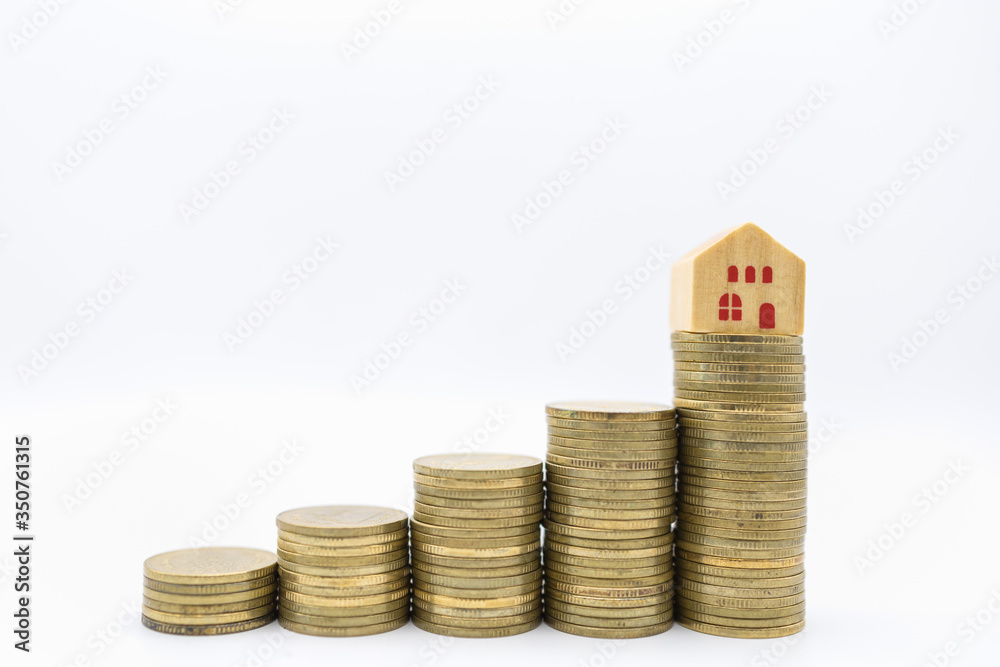 Business, Money, Home Loan and Saving Concept. Closeup of mini wooden house toy on top of stack of gold coins on white background. Business, Money, Home Loan and Saving Concept. Closeup of mini wooden house toy on top of stack of gold coins on white background.