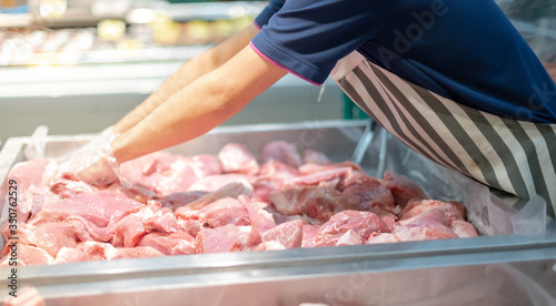 The supermarket employee preparing the Fresh pork meat slice on display tray for consumers select in a supermarket.