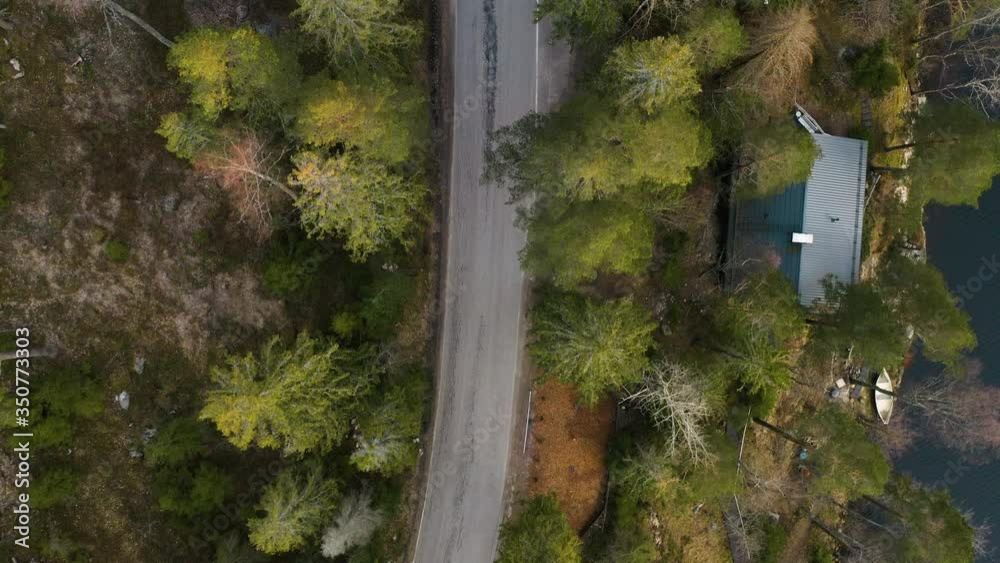 A top-down view from a drone flying over a town road found in the middle of a hilly forest next to a river. A top-down view from a drone flying over a town road found in the middle of a hilly forest next to a river.