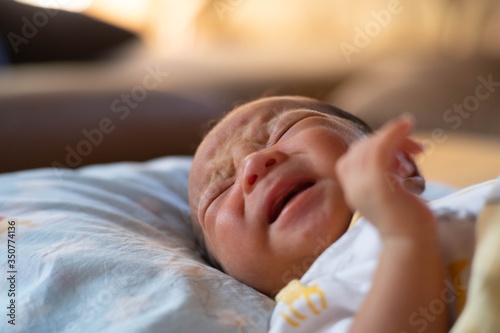 The adorable cute newborn baby infant lying on the bed and cry colic