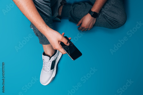 Young guy sitting on the floor in his hands holding smart phone, correspondence by phone, search on the Internet, read e-books