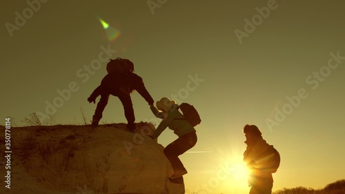 climbers travelers climb mountain holding out helping hand to each other. joint work of tourists. joyful tourists jump and wave their hands. trip to mountains at sunset. businessmen teamwork