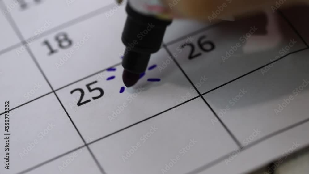 Mark the 25th day of the month on the calendar with a blue pencil. Female hand draws the sun and the wavy sea on a calendar. Date of event, important day of the month.