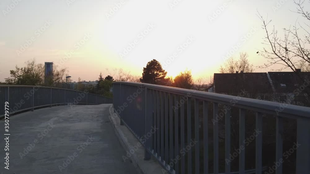 Drone starting flight from a bridge filming into the setting sun with buildings and private homes in the shadows of the dying sunlight in Europe Drone starting flight from a bridge filming into the setting sun with buildings and private homes in the shadows of the dying sunlight in Europe