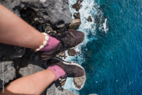 Girl sitting on the edge of the cliff, legs hanging down over the ocean, view from the top, dangerous 