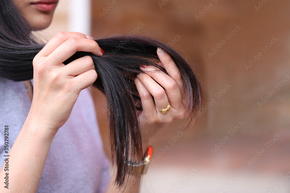 Naklejka premium Woman hand holding her long hair with looking at damaged splitting ends of hair care problems