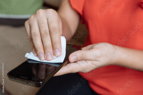 Woman's hands wipe smartphone screen with disinfectant cloth. Close-up woman cleans her mobile phone at home. Coronavirus pandemic