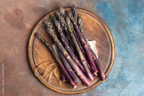 Natural organic purple asparagus vegetables on a wooden board on a dark stone background. photo