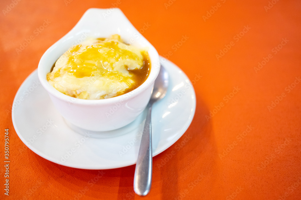 A cup of mashed potato and cheese on top with spoon put on red table background A cup of mashed potato and cheese on top with spoon put on red table background