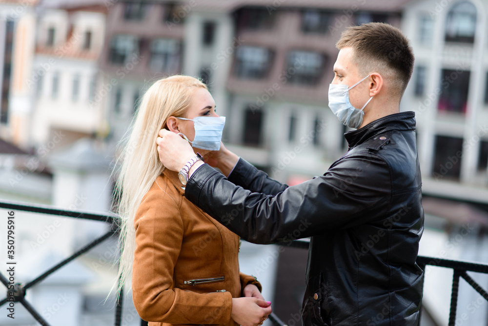 Fototapeta premium Young couple in love in protective medical mask on face outdoor at street. Environmental pollution concept. Guy and girl in virus protection
