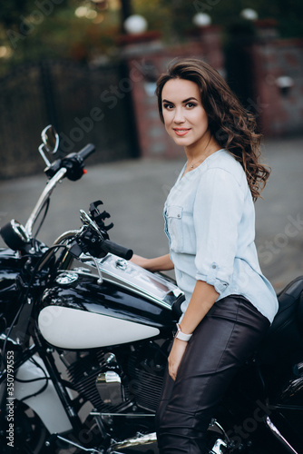 Young beautiful biker woman in a blue shirt on a motorcycle. The concept of speed and freedom. Soft selective focus. © Tasha Sinchuk