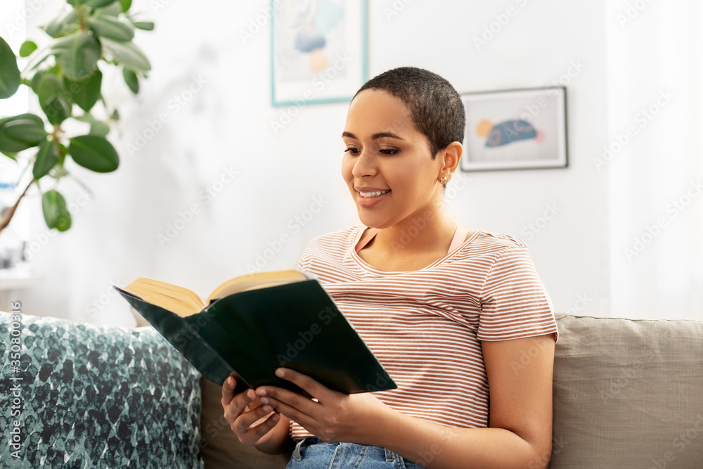 people and leisure concept - happy smiling african american woman sitting on sofa and reading book at home people and leisure concept - happy smiling african american woman sitting on sofa and reading book at home