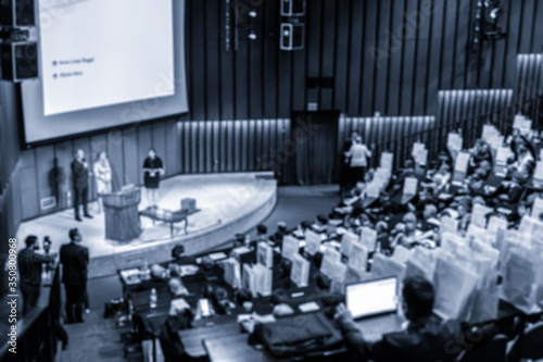 Defocused image of speakers giving a talk at business meeting. Audience in the conference hall. Business and Entrepreneurship concept. Blue toned.