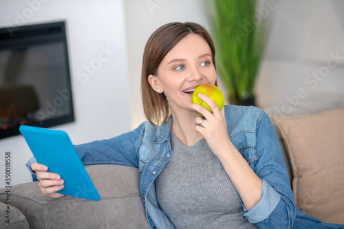 Young pregnant woman in a jeans jacket eating apple
