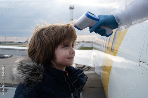 Safety and health during a pandemic of corona virus. Covid 19 coronaviruse protection. Stewardes measures the body temperature of child before boarding a plane. A boy near the plane and a thermometer. photo