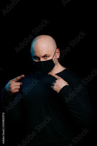 A bald man in a black virus mask on a black background. Protection and prevention from infection. Portrait of a serious man in a dark key.