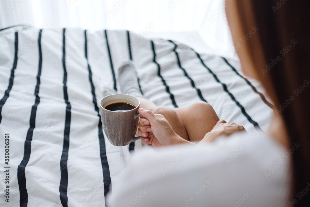 A beautiful woman drinking hot coffee in a white cozy bed at home in the morning A beautiful woman drinking hot coffee in a white cozy bed at home in the morning