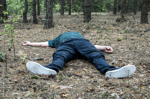 Murder in the woods. The body of a man in a blue t-shirt and trousers lies on the ground among the trees in the forest. Victim of an attack.