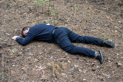 Murder in the woods. The body of a man in a blue shirt and trousers lies on the ground among the trees in the forest. Victim of an attack.