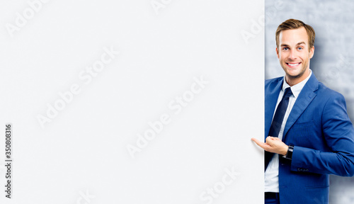 Businessman showing blank signboard, standing over white bricks wall background. Empty copy space area for slogan or some advertising text. Business and education concept.
