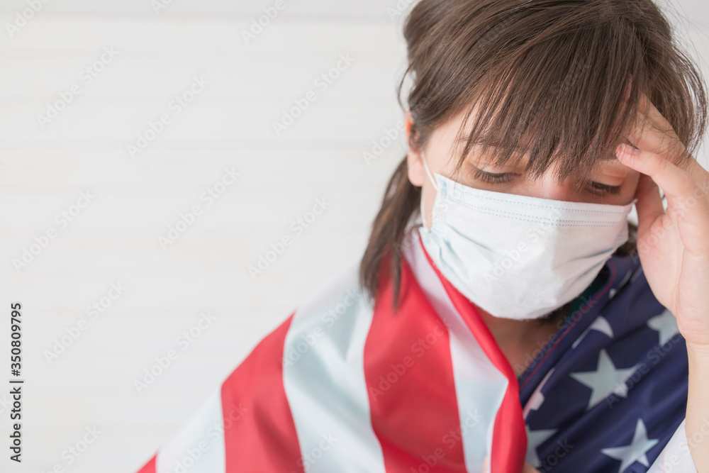 A woman in a medical mask wrapped herself in the US flag. America's Emergency Regime Due to COVID-19 Pandemic A woman in a medical mask wrapped herself in the US flag. America's Emergency Regime Due to COVID-19 Pandemic