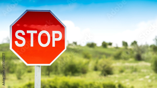 Red stop sign in the middle of empty fields. Left part of the frame. Blue cloudy sky.