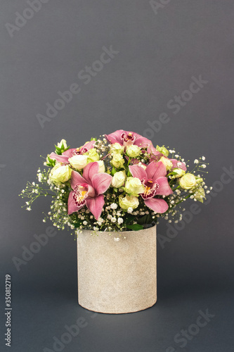 Vase with beautiful bouquet of orchids, roses and gypsophila, Baby's-breath flowers, on dark grey background with copy space for your text. Selective focus, celebrating concept