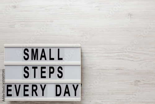 Fototapeta Naklejka Na Ścianę i Meble -  'Small steps every day' words on a modern board on a white wooden surface, top view. Overhead, from above, flat lay. Copy space.
