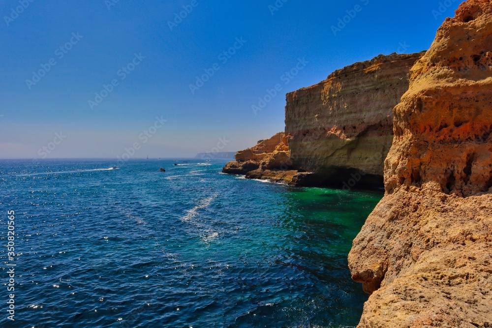 View from Algar Seco Cave in Carvoeiro. Colorful cliffs beautiful turquoise Atlantic ocean with little boats in the distance in Algarve.