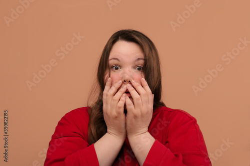 Beautiful young girl look with a frightened expression on her face. Beige background.