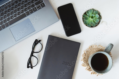White flatlay of desktop with phone mockup and coffee cup, morning breakfast,plant,  scedualing in 2020