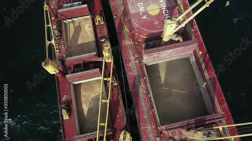 Top view bulk carrier deck and barge filled with coarse grain, soybean or wheat. Process of underway ship to ship transfer operation in open sea. Cargo freighter load transport oats on another vessel