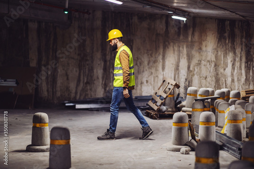 Full length of handsome worker walking around underground garage in construction process.