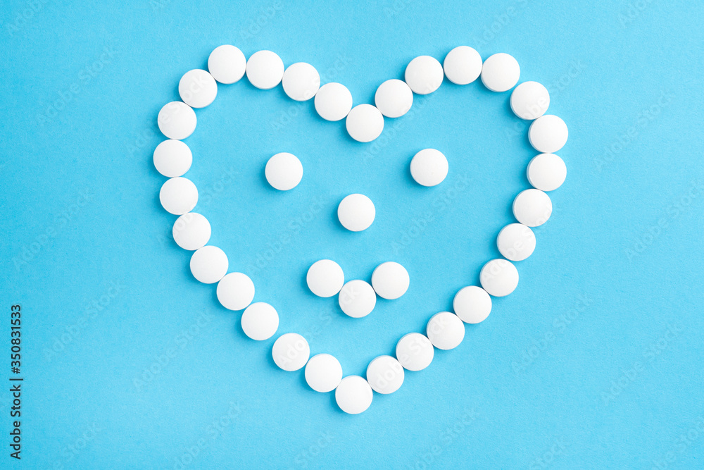 Heart shaped smile made from white medical pills on blue paper background. The concept of sedative drugs and recovery Heart shaped smile made from white medical pills on blue paper background. The concept of sedative drugs and recovery