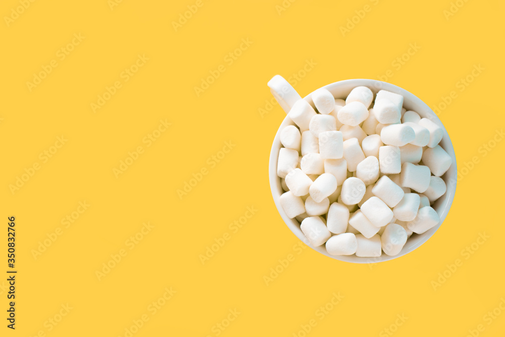 Small white marshmallows in a white Cup on a yellow background Small white marshmallows in a white Cup on a yellow background