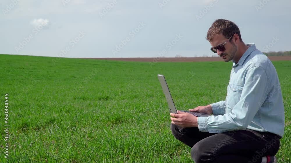 Farmer with laptop inspects wheat growth. Fresh green wheat field Farmer with laptop inspects wheat growth. Fresh green wheat field
