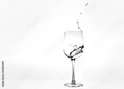 Water in a wine glass. Splash of liquid on a white background. Isolated object. Spray. Copy space for text. Selective focus.