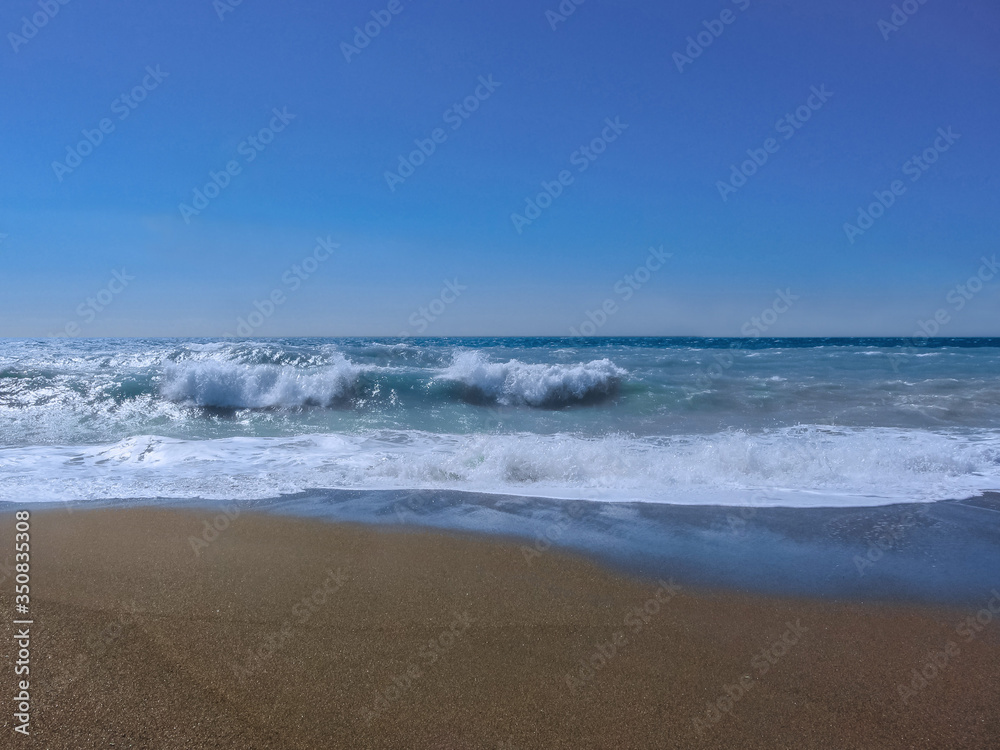 Blue stormy sea with blue sky and dark sand.
