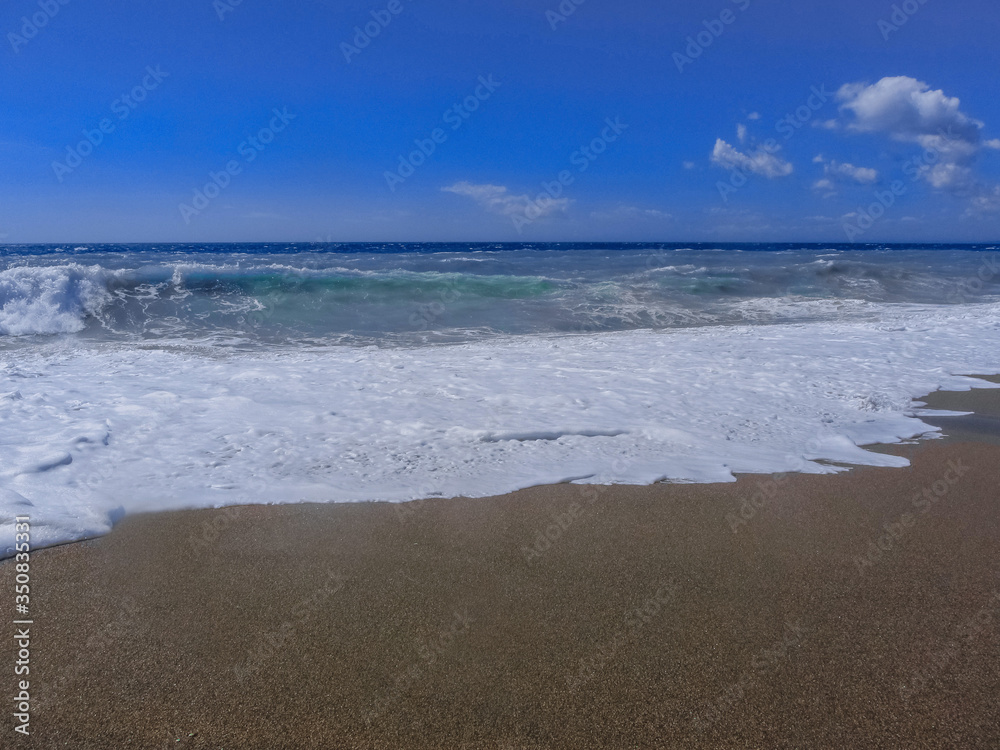 Fototapeta premium Blue stormy sea with blue sky and dark sand.
