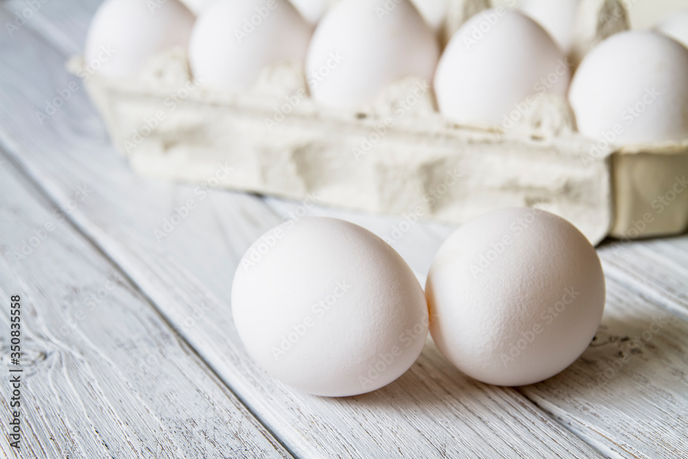 Close-up of fresh white organic chicken eggs in the paper tray on light wooden background Close-up of fresh white organic chicken eggs in the paper tray on light wooden background