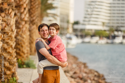 Son & father walking on a beach near palm trees weared in casual clothes. Tropic vacation. Sea relax and rest. Spending a time on a beach. Smiling boy with his Dad together. Summer holiday sunny day