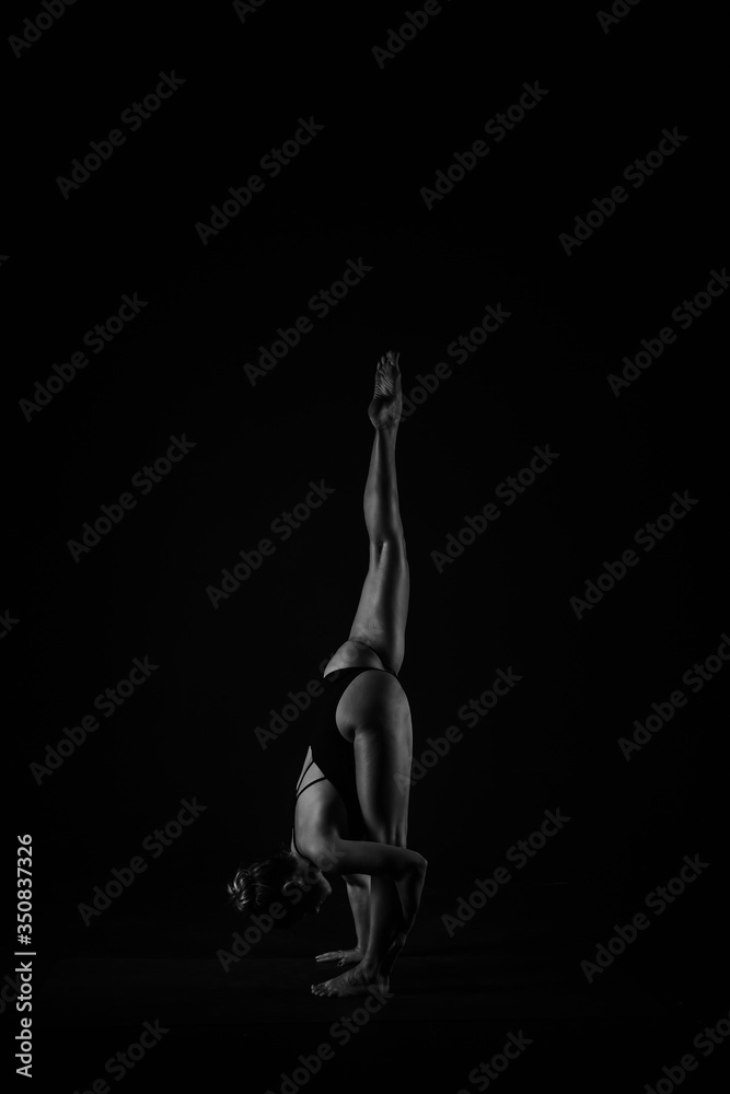 Girl yogi performs exercises on a black background. The flexibility of the female body. Asana. Relief of the muscles. Figures from the body.