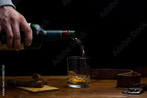 whiskey being poured into a glass in a moody scene with cigars