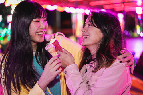 Happy asian girls eating candy sweets ice cream at amusement park - Young trendy friends having fun together- Tech, friendship and millennial generation concept - Focus on faces