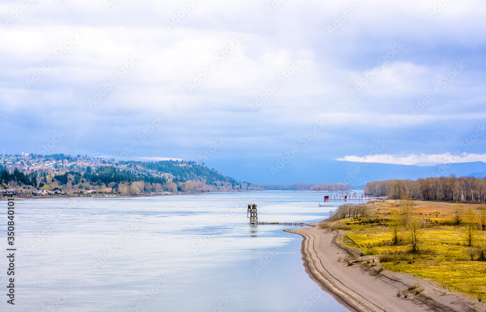 Columbia River landscape with cloudy sky and hills with trees and houses and marinas for fishing schooners in Columbia Gorge