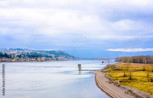 Fototapeta Naklejka Na Ścianę i Meble -  Columbia River landscape with cloudy sky and hills with trees and houses and marinas for fishing schooners in Columbia Gorge