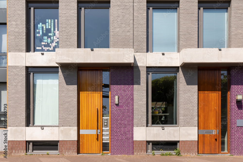 Exterior facade of a house with different colored purple stones an warm brown colored wooden doors. Modern Dutch houses in Brabant, the Netherlands